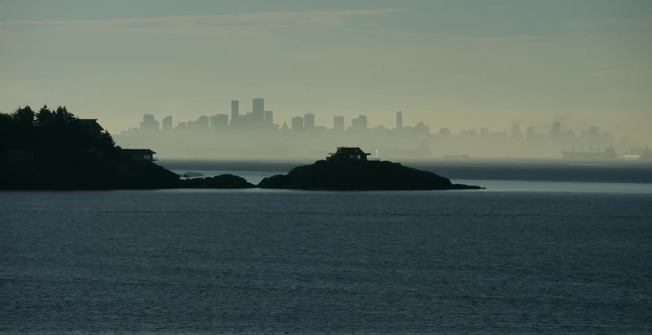 A body of water sits in front of city skyscrapers on a misty day