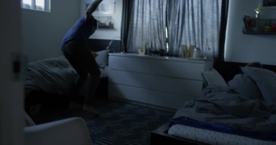 A man walks down a dark hall entering a bedroom to wake someone up