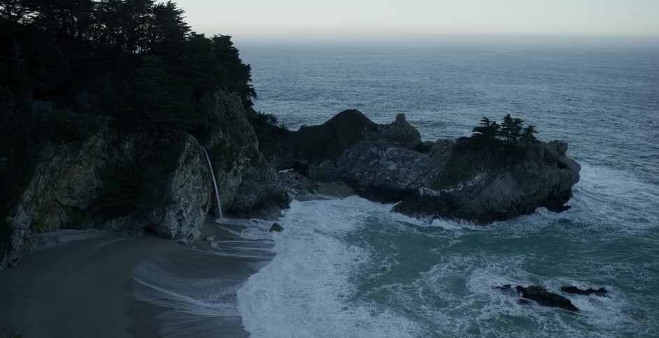 Waves roll up on a shore near a rocky overhang