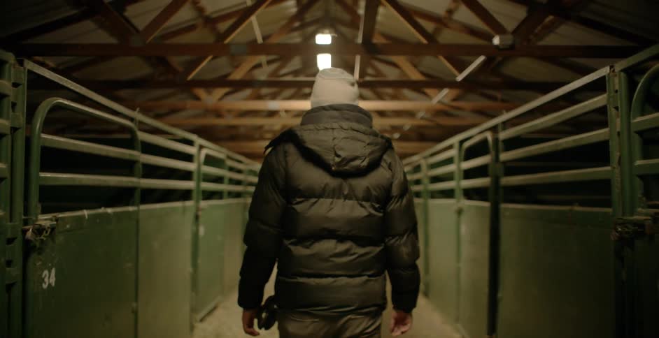 A man is walking through a barn lined with metal stalls