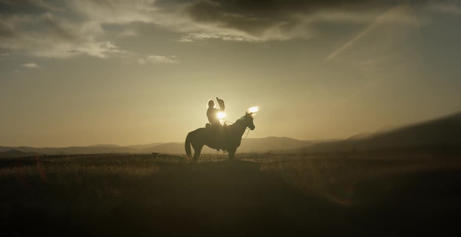 Man sitting on horse puts cowboy hat on at sunset