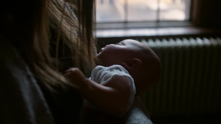Woman standing and cradling sleeping baby in room during the day