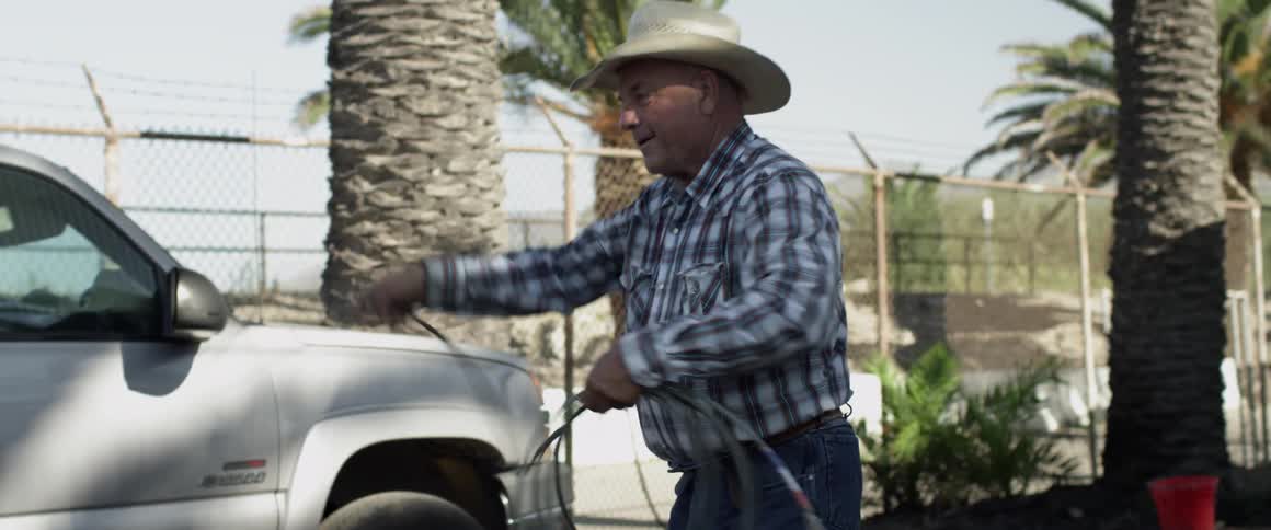 Man waves a lasso over his head outside near palm trees