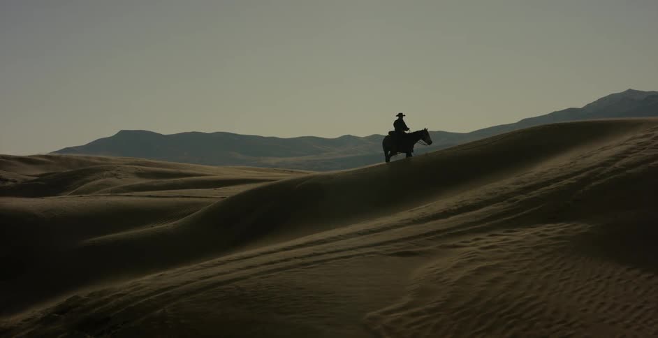 Man riding horse over sand dunes on windy evening