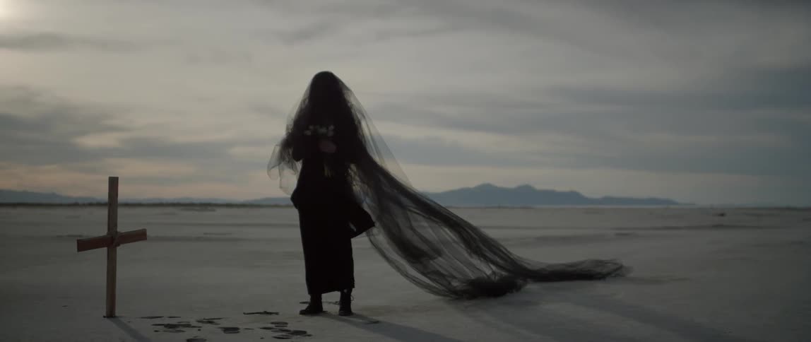 Woman wearing a long black veil stands next to a grave