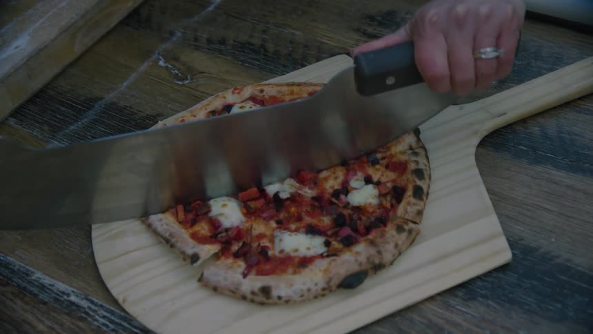 A man cuts a pizza on a board with a pizza cutter