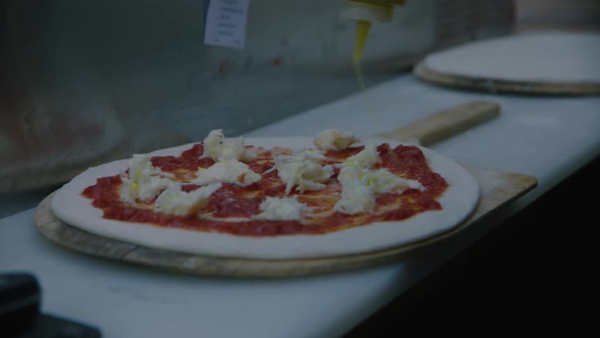 Person puts sauce on an uncooked pizza on a paddle