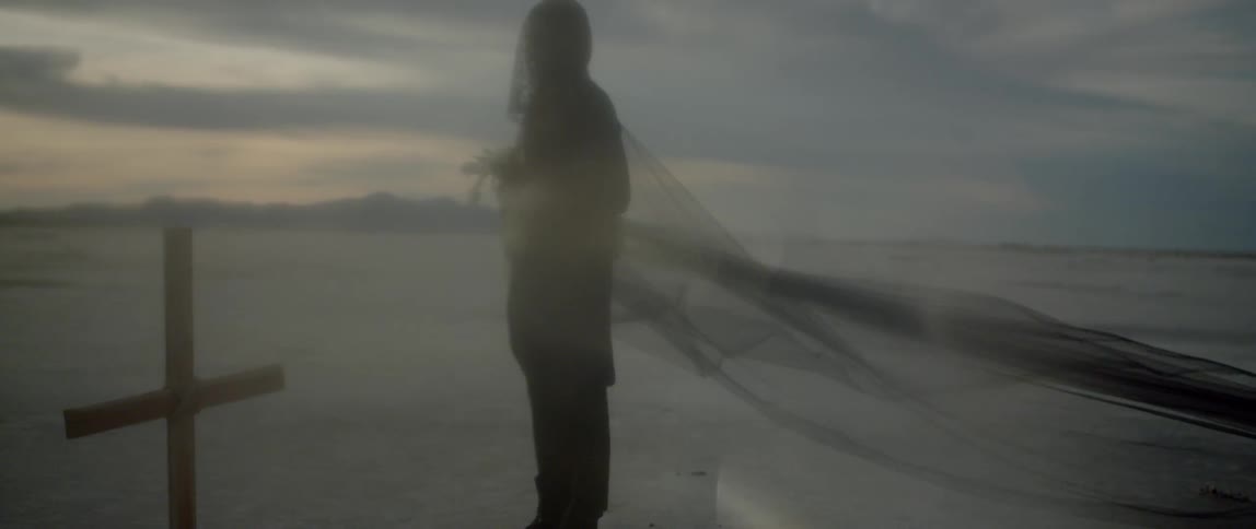 Woman wearing a long black veil stands next to a grave