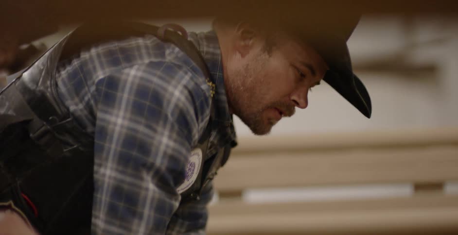 Man wearing cowboy hat leans over a gate