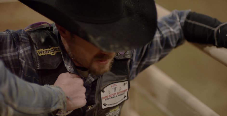 A rodeo worker holds onto a cowboy sitting and waiting for the starting bell