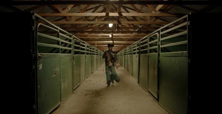 A rodeo cowboy is walking in hall lined with horse pens