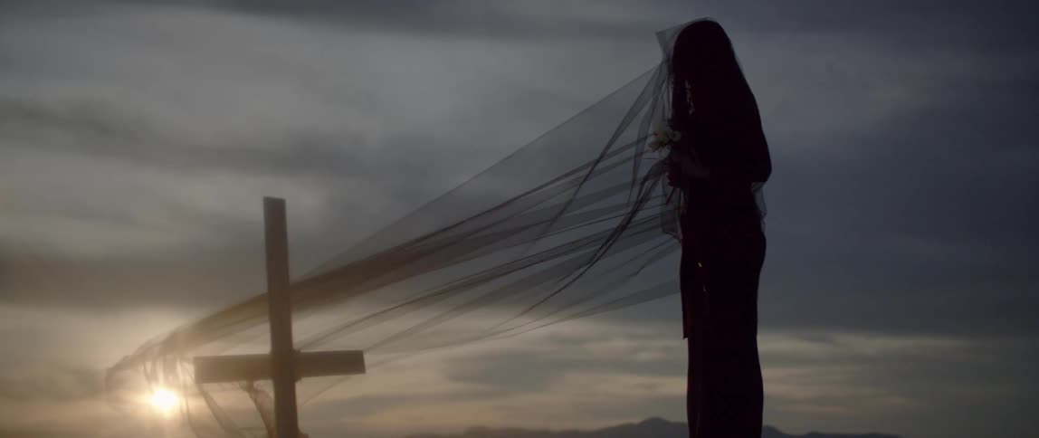 A woman grieves in front of a cross