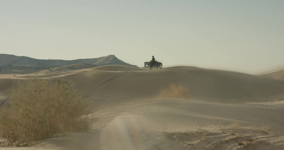 A person is riding a horse over sand dunes during the day