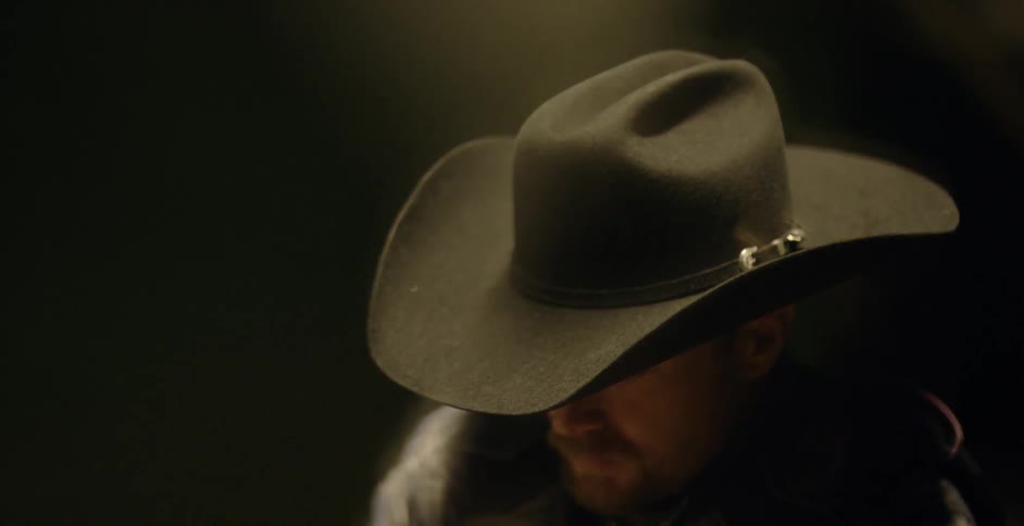 A man stands unmoving in a cowboy hat
