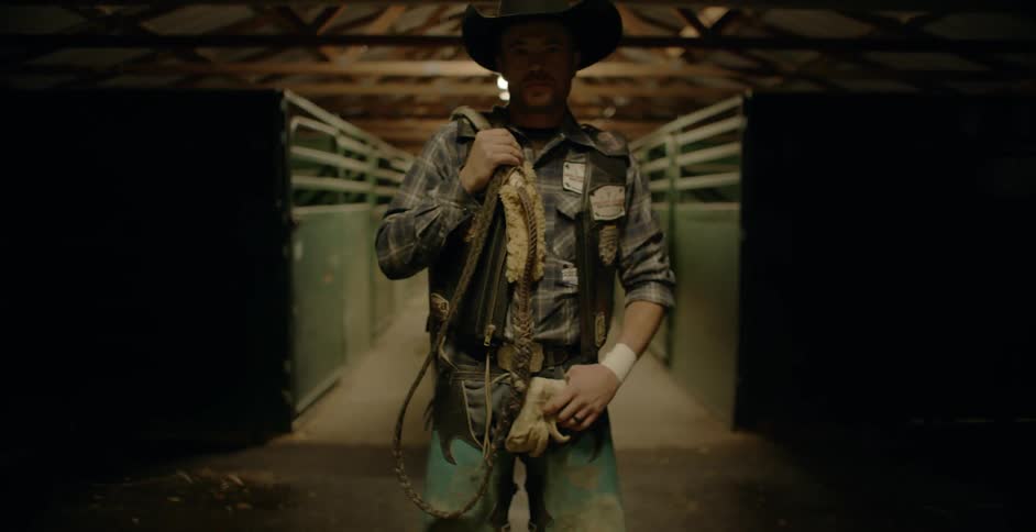 A rodeo cowboy carrying rope stands in front of stalls