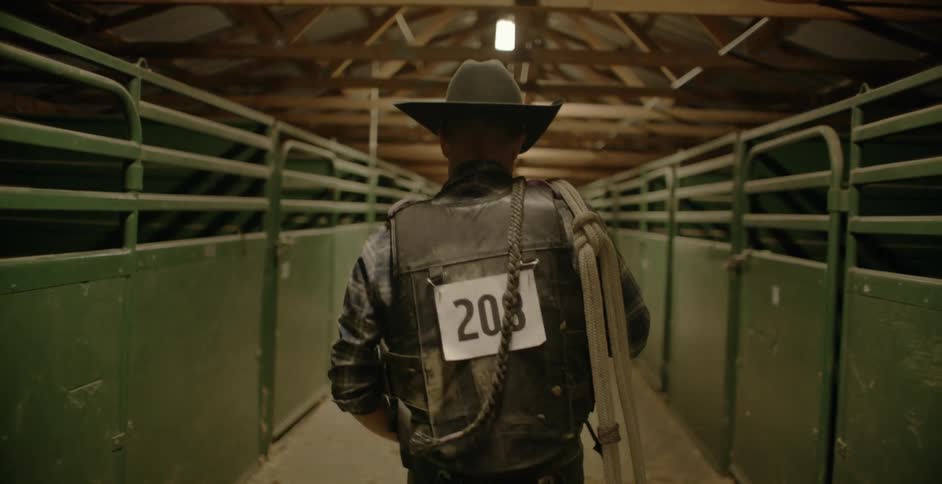 Man carrying a rope walks in a barn past stalls
