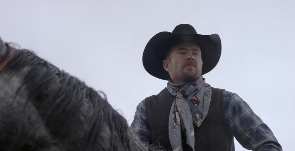 Man wearing a hat sits on a horse in the rain
