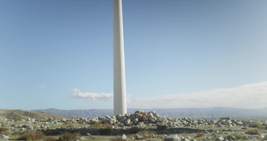 A child plays on the rocks beneath a wind turbine