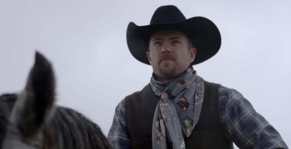 Man wearing cowboy hat sitting on horse outside while snow falls