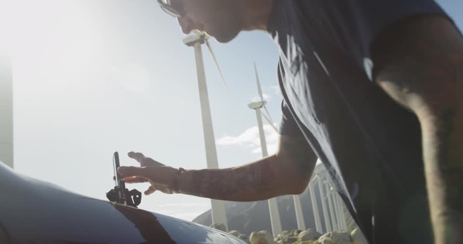 Man grabs phone off of a car hood in front of a row of windmills