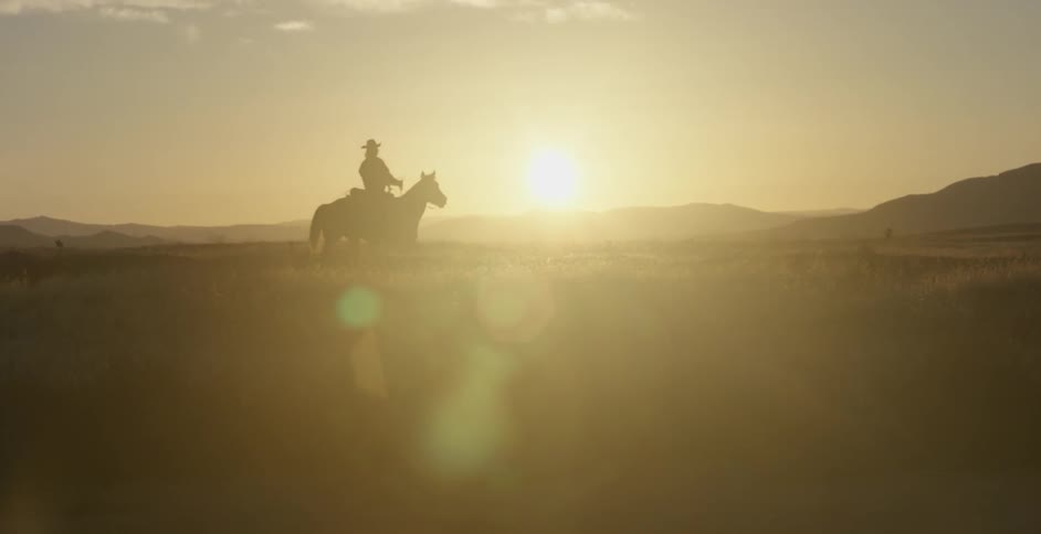 A cowboy rides a horse in a rural area at sunset