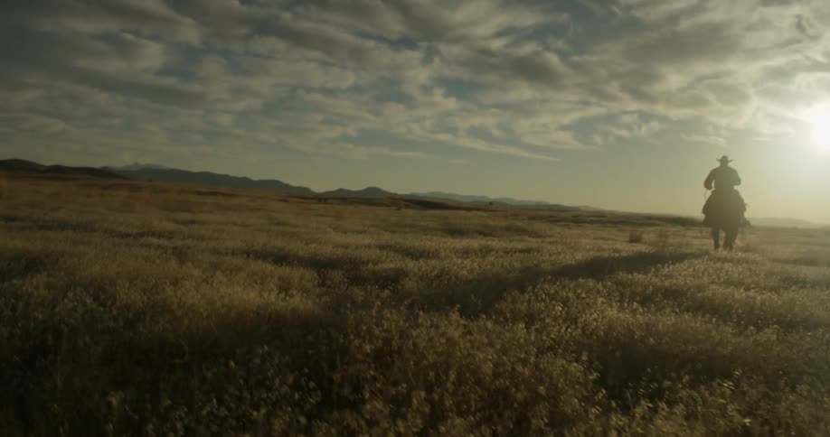 A cowboy is riding his horse over a grassy plain on a cloudy day