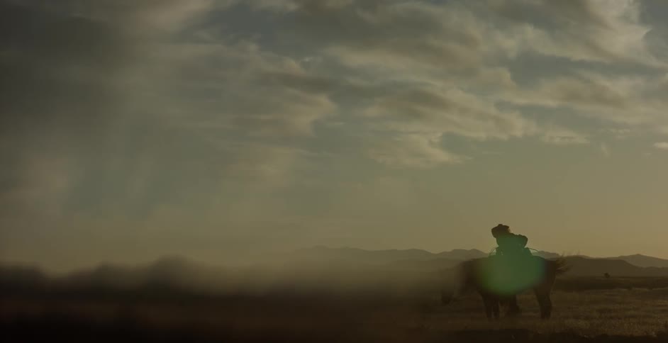 Man mounts and rides horse on cloudy evening while dog follows