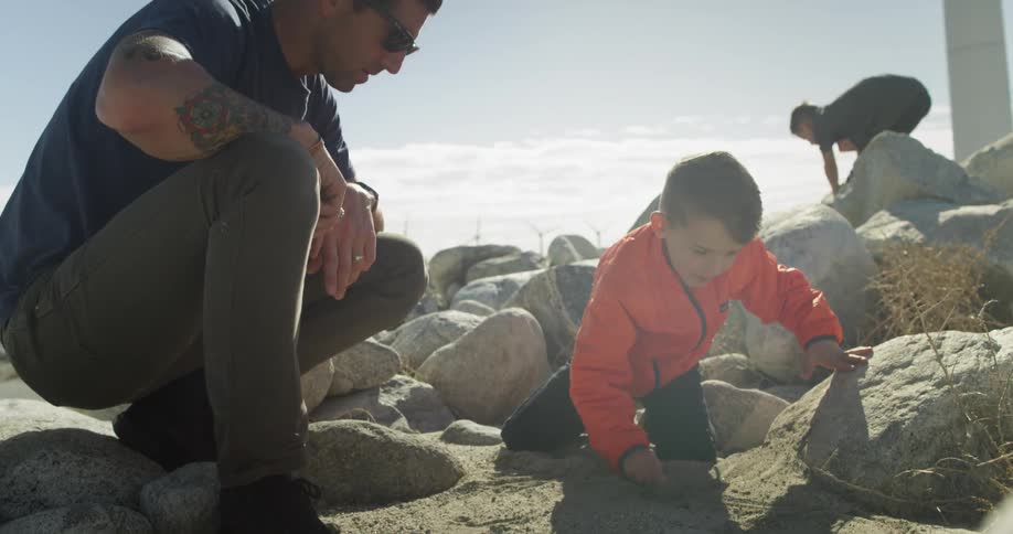 A father watches as his young son plays in the dirt and rocks