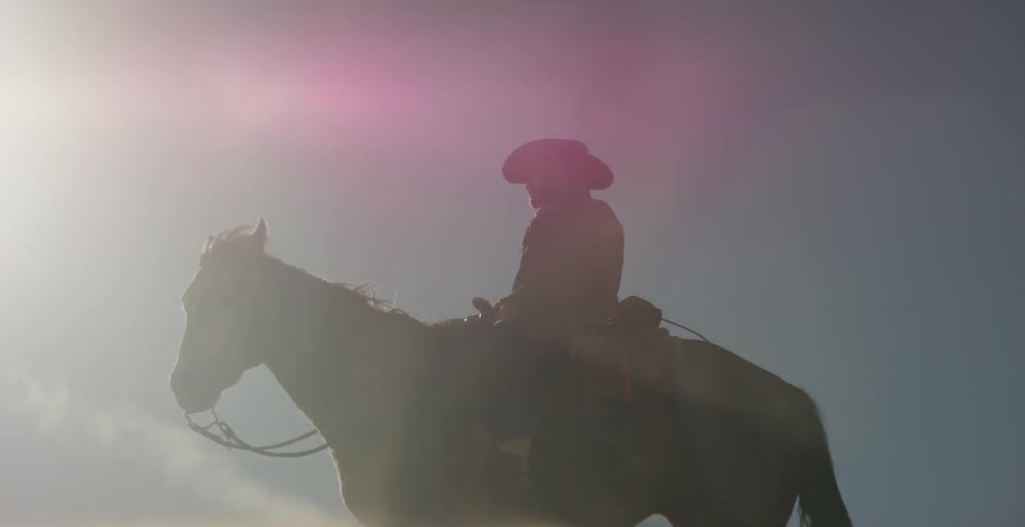 Man sits on a horse in the sun with dust blowing