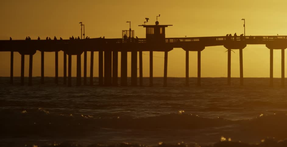 People stand on an ocean pier as waves flow towards the shore