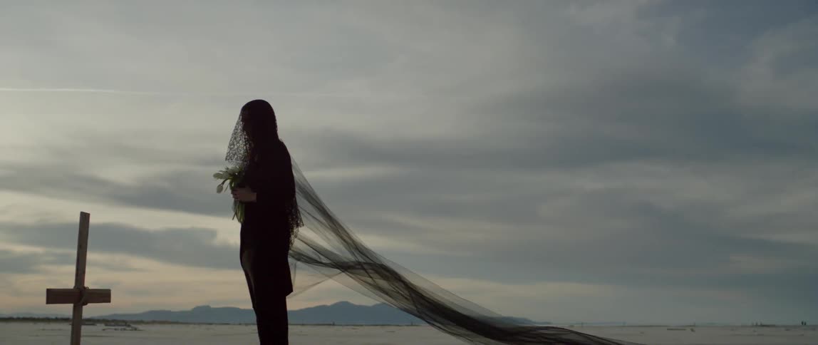 Woman wears long black veil while holding white flowers