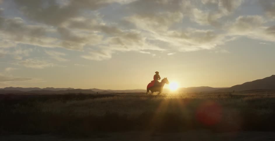 A man rides a horse towards the sunset