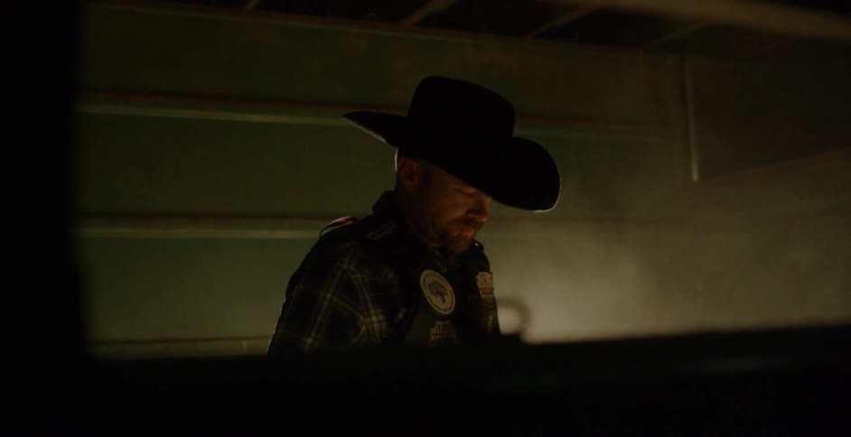A rodeo cowboy angrily paces back and forth in a horse stall