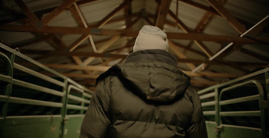 A man is walking in a hall with lined with horse pens