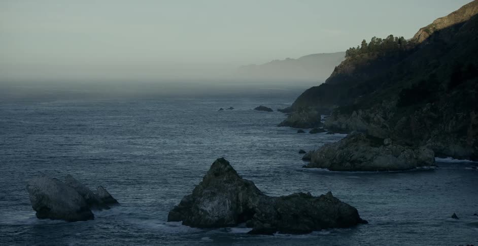 A bunch of large rocks resting in the ocean with fog in the background