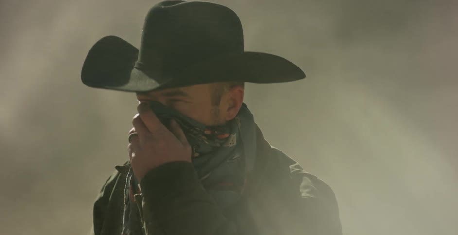 A cowboy pulls his bandana up over his mouth to keep out the dust