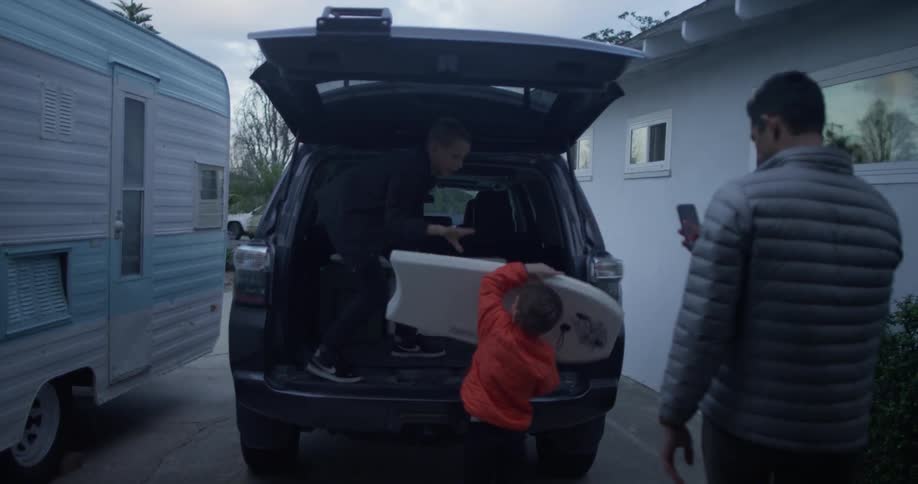 Child puts swimming boards in a vehicle while a man takes pictures