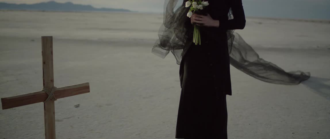 A woman in black stands near a cross marking a grave