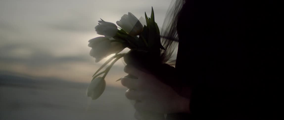A woman is holding a bunch of white flowers as she stand outside