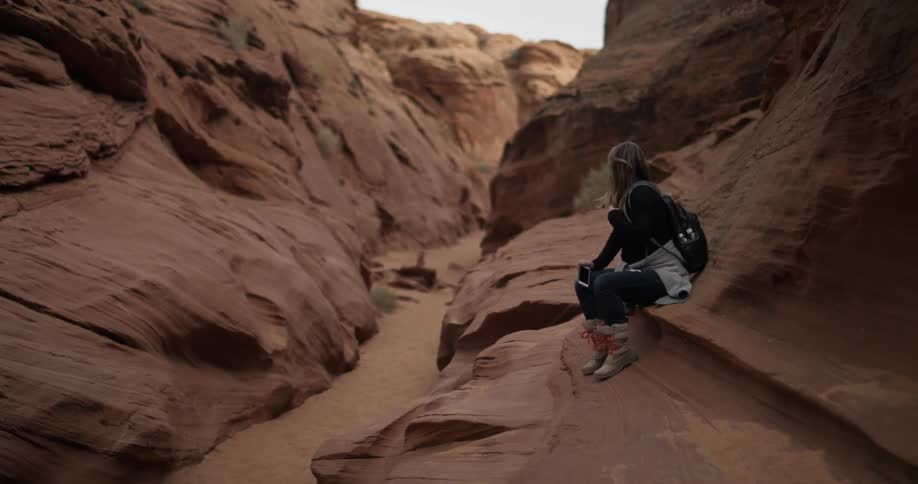 A woman sits on an orange rock in a canyon