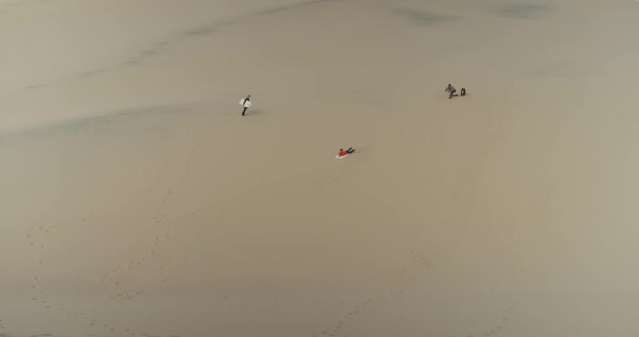 A few people sliding down hill on sand on a sled