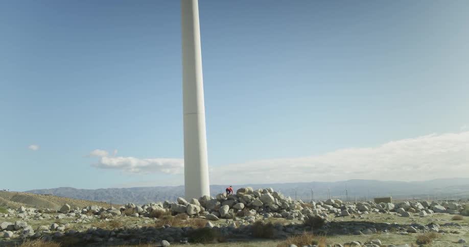 Person climbs up a pile of rocks next to a large white pole