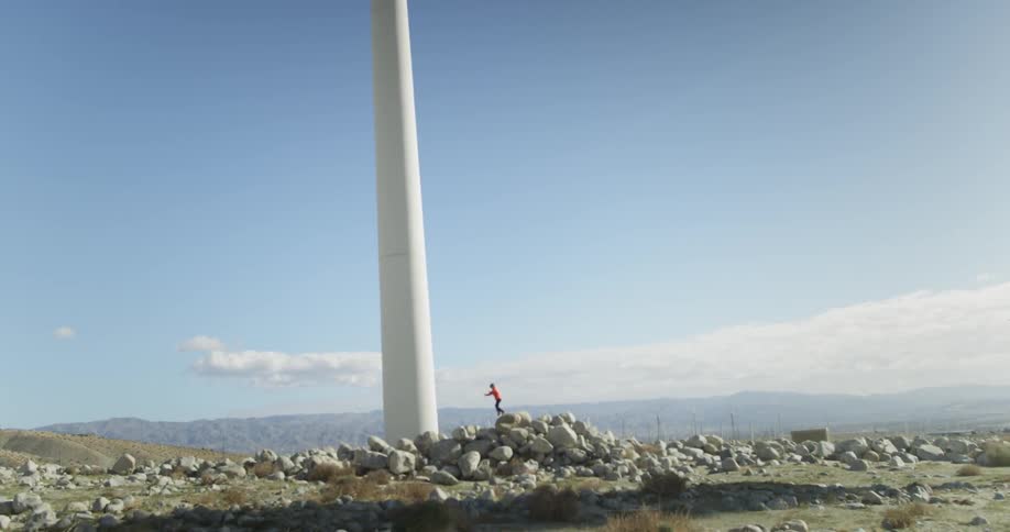 A kid standing on a large pile of rocks near a big pole
