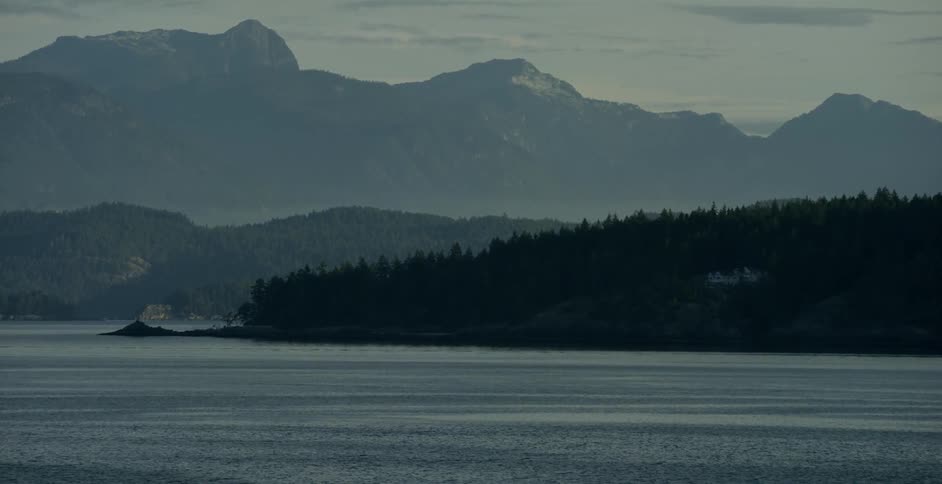 Water ripples and laps the shoreline of a mountainous area in late afternoon