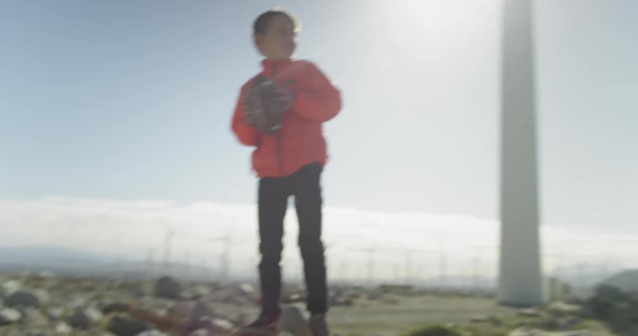 A young boy throws a football as he stands on some rocks