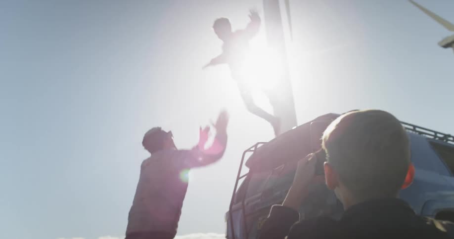 A young boy jumps from a top a truck into his father's arms