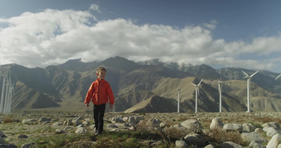 A boy playing near wind turbines throws a football
