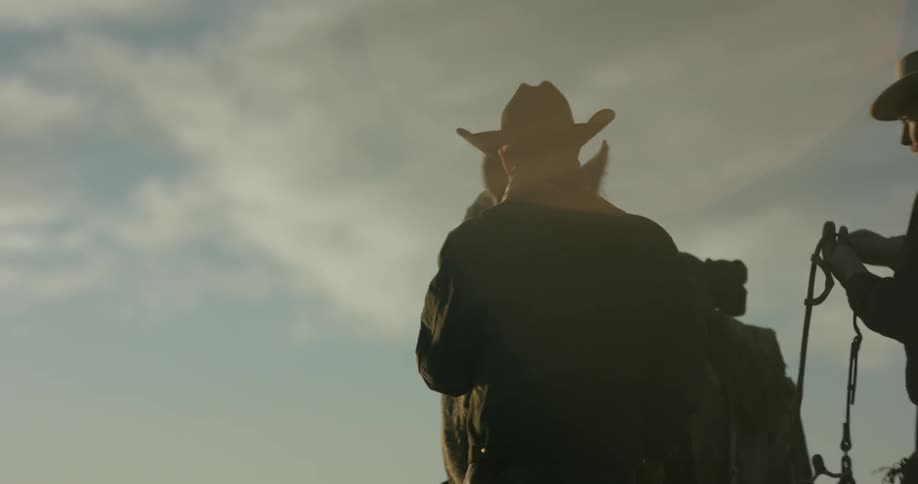 A cowboy pats a horse's face as another adjusts a strap