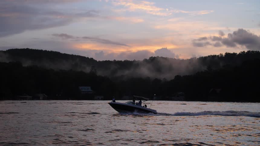 Boat traveling in a lake with treeline in the background