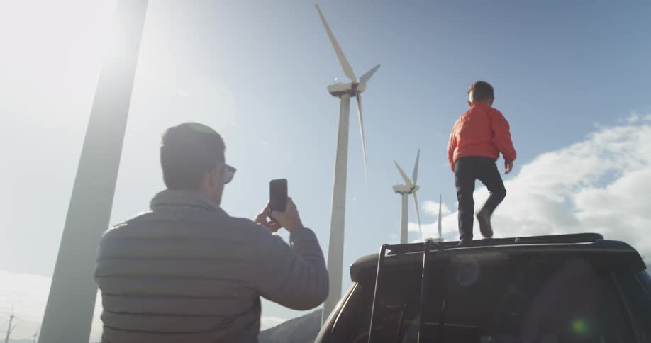 A man is filming a young boy climbing up onto the top of an suv